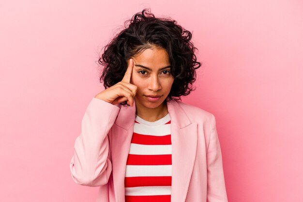 Joven mujer latina de moda aislada sobre fondo rosa señalando la sien