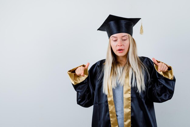 Fille Blonde En Robe De Graduation Et Casquette Pointant Vers La Caméra