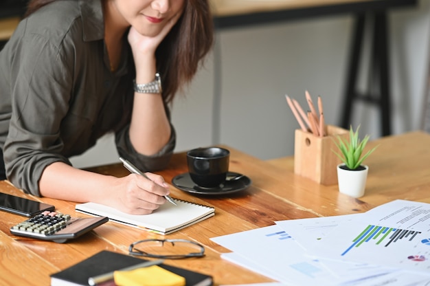 Cropped strzału żeński writing na notatniku i finanse dane na stole. Premium Zdjęcia