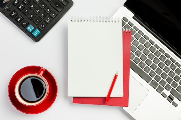 Czerwona filiżanka, kalkulator, ślimakowaty notepad, ołówek na laptopie nad białym tłem Darmowe Zdjęcia