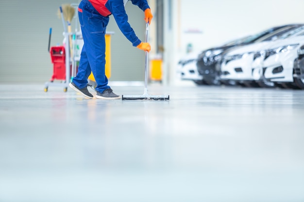 Czyszczenie centrum serwisowego mechaników samochodowych za pomocą mopów do spuszczania wody z posadzki epoksydowej. w centrum serwisowym naprawy samochodów. Premium Zdjęcia