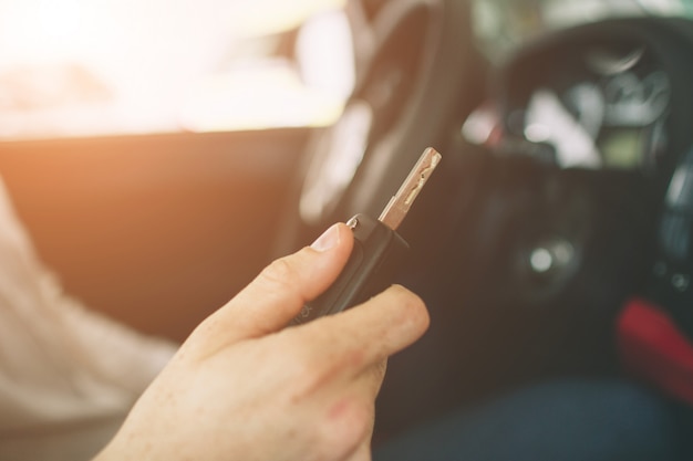 Dłoń Trzymająca Kluczyk Z Pilotem, Z Nowoczesnym Samochodem. Mężczyzna Siedzący Wewnątrz Nowego Samochodu Z Kluczami. Premium Zdjęcia