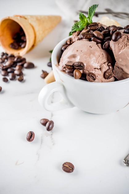 Domowe lody kawowe, podawane z ziarnami kawy i liśćmi mięty, z szyszkami lodów i łyżkami na zdjęciu. tło z białego marmuru, Premium Zdjęcia
