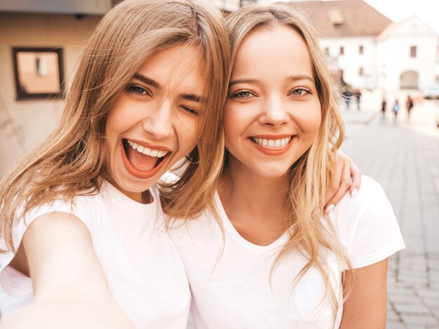 Dwie Młode Uśmiechnięte Hipster Blond Kobiety W Letnie Białe Ubrania Ubrania. Dziewczyny Robienia Zdjęć Autoportretów Selfie Na Smartfonie. . Darmowe Zdjęcia