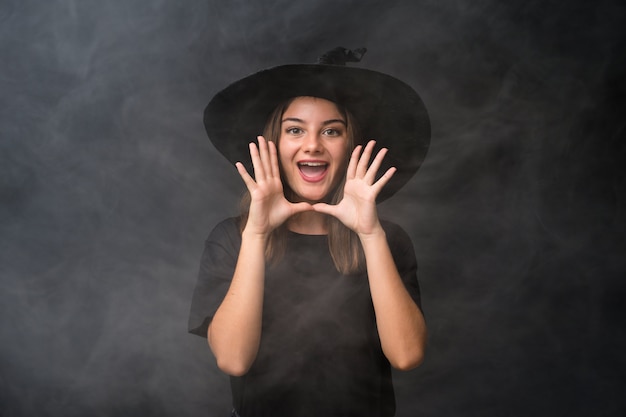 Dziewczyna z kostiumem wiedźmy na imprezy halloween na pojedyncze ciemne ściany krzyczy z szeroko otwartymi ustami Premium Zdjęcia