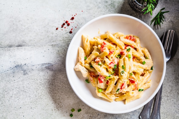 Makaron Penne Z Kurczakiem, Pieprzem I Zieloną Cebulą W Kremowym Sosie W Białym Talerzu, Szare Tło, Widok Z Góry. Premium Zdjęcia