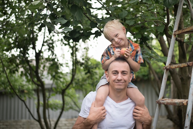 Mały blond chłopiec z jabłkiem w rękach na ramionach ojca. Premium Zdjęcia