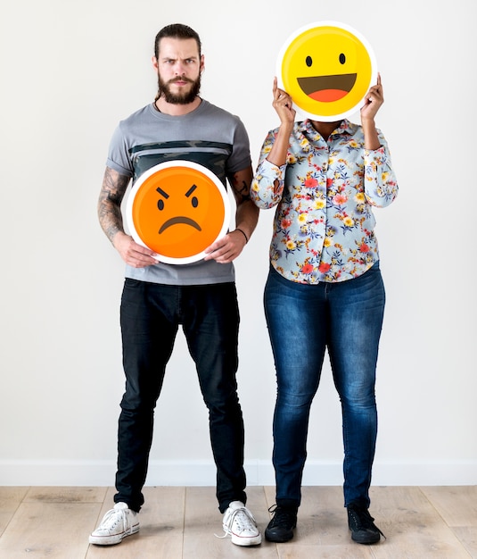 Międzyrasowa para trzyma ekspresyjnego emoticon twarzy wyraz twarzy marszczy brwi i uśmiech relacje Premium Zdjęcia