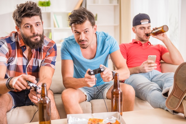 Młodzi mężczyźni piją piwo, jedzą pizzę i grają w gry Premium Zdjęcia