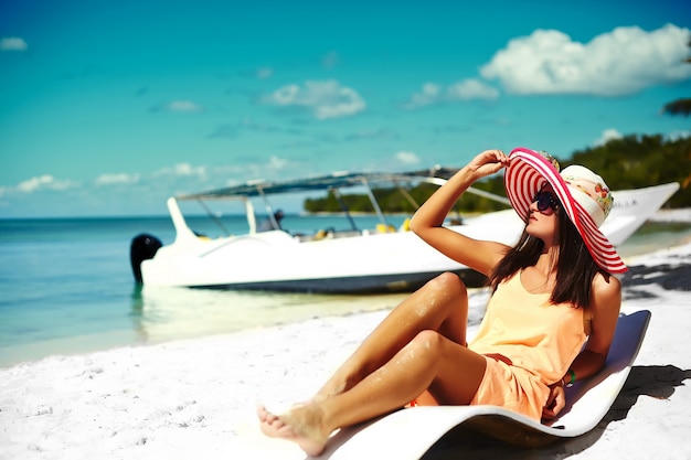 Piękna Kobieta Model Opalając Się Na Krześle Plaży W Białym Bikini W Kolorowe Sunhat Za Niebieski Lato Wody Oceanu Darmowe Zdjęcia