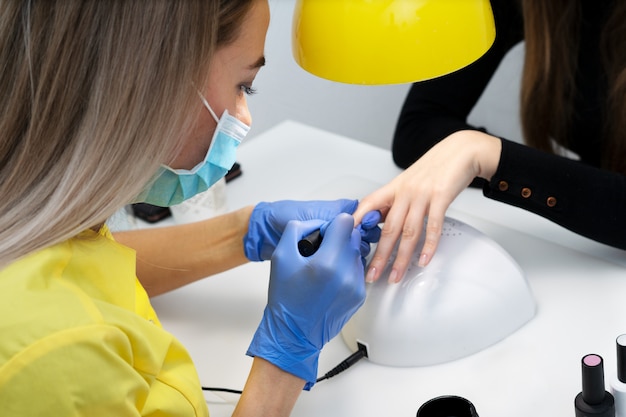 Pielęgnacja Paznokci. Manicure W Salonie. Mistrz Pielęgnuje Dziewczynę, Piękno I Zdrowie. Proces Manicure. Mistrz W Maskach I Rękawiczkach. Lakier Do Paznokci Premium Zdjęcia
