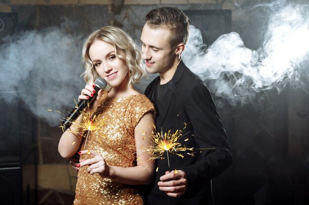 Portret szczęśliwa potomstwo para śpiewa z mikrofonem z sparklers. Premium Zdjęcia