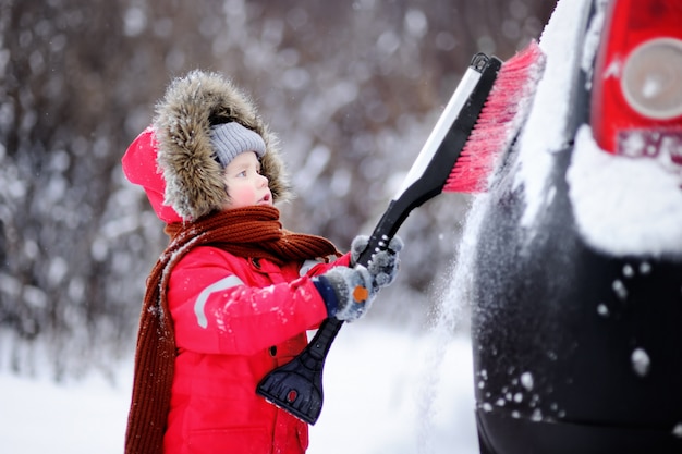Słodkie małe dziecko pomaga szczotkować śnieg z samochodu. toddler chłopiec za pomocą narzędzia do czyszczenia samochodu ojców Premium Zdjęcia