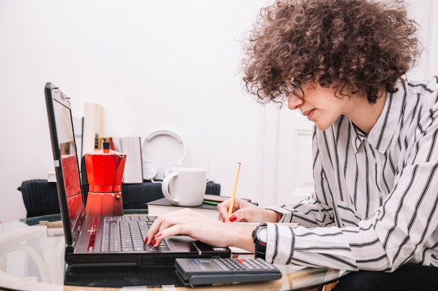 Adolescente usando la computadora portátil y haciendo notas Foto Gratis