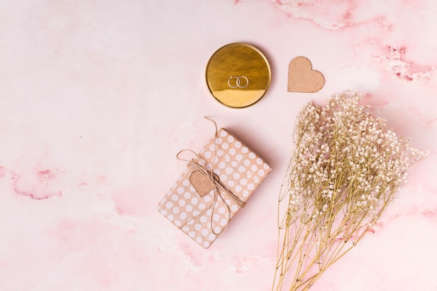 Adorne el corazón cerca del manojo de flores, presente cuadro y anillos en redondo Foto gratis