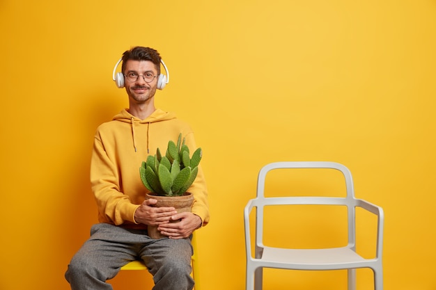Alegre Hombre Sin Afeitar Escucha Música En Auriculares Estéreo Sostiene Cactus En Macetas 8316