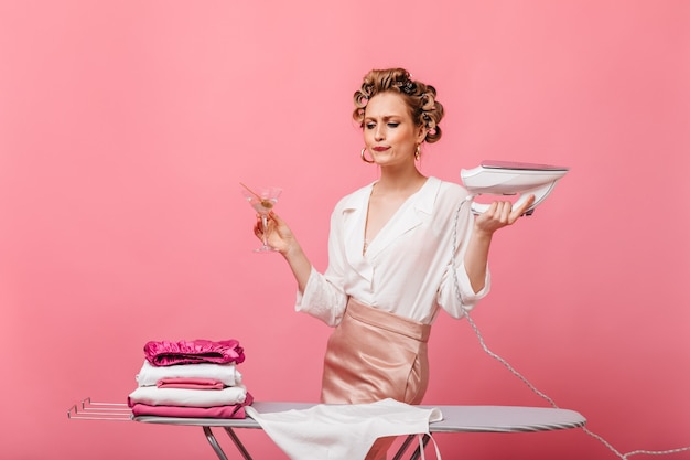 Ama de casa joven en traje elegante posando con plancha y martini en