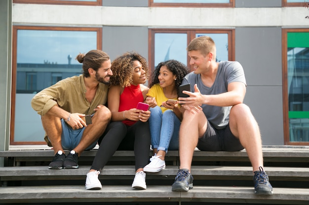 Amigos alegres felices leyendo noticias en las pantallas del teléfono Foto gratis