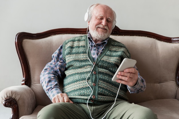 Anciano de alto ángulo en el sofá tocando música en el móvil Foto gratis