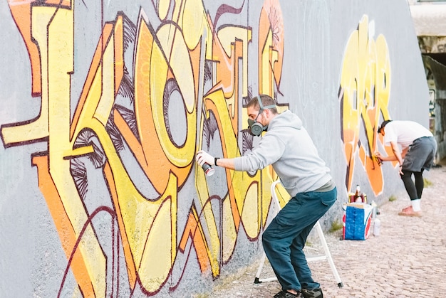 Artistas De Graffiti Pintando Coloridos Murales En Una Pared Gris