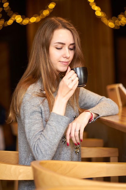 Atractiva Mujer Encantadora Encantadora Con Cabello Largo Maquillaje Natural Y Sonrisa Amistosa En El Cafe Y Sosteniendo Una Taza De Cafe Negro Foto Premium