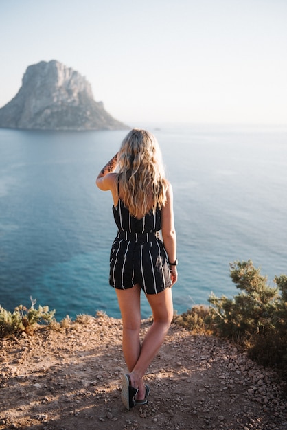 Atractiva mujer joven de pie sobre un acantilado junto al hermoso mar durante el día Foto gratis