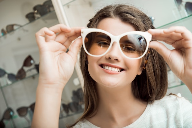 Bonita Chica Morena Sonriendo Probandose Gafas De Sol En La Tienda De Optica Foto Gratis