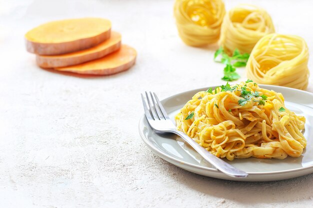 Calabaza alfredo fettucine pasta en un plato de cerámica con rodajas de calabaza cruda fresca. comida de otoño para el almuerzo. receta de calabaza moscada. Foto gratis
