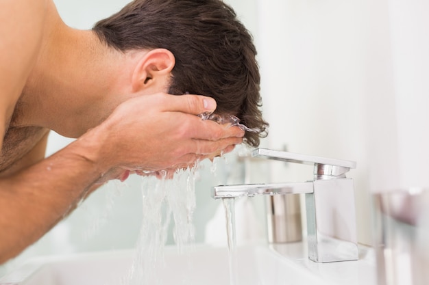 Sin camisa joven lavando la cara en el baño | Foto Premium