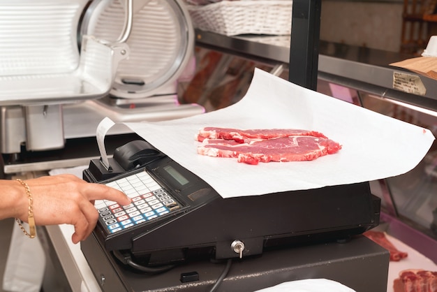 Carnicero que pesa carne en vitrina en la carnicería | Foto Premium