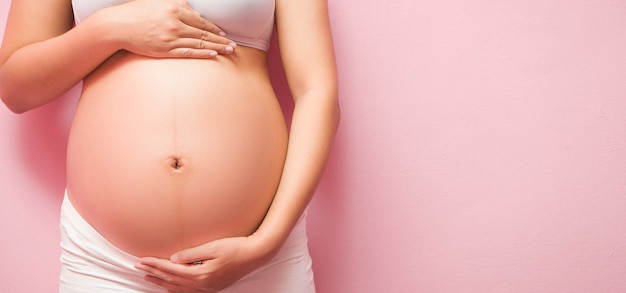 Cerca de vientre embarazado sobre fondo rosa Foto Premium 
