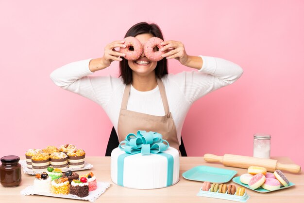 Chef pastelero con un gran pastel en una mesa sobre pared rosa aislado