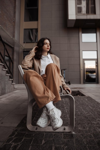 Chica alta y elegante con chaqueta de gran tamaño sentada en el banco