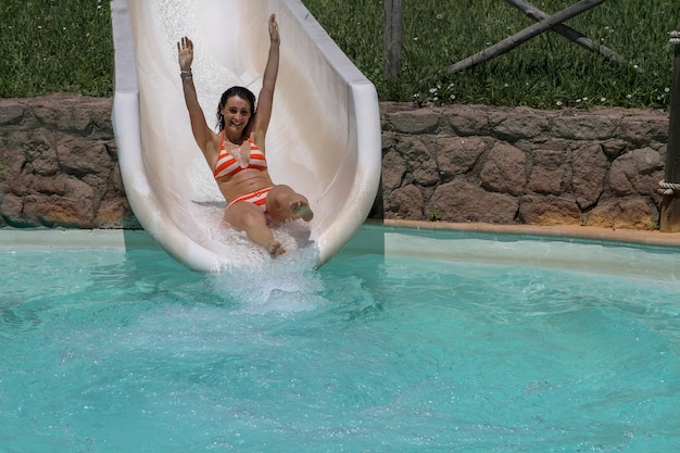 Chica en bikini divirtiéndose al caer por el tobogán de agua en el parque acuático Foto Premium