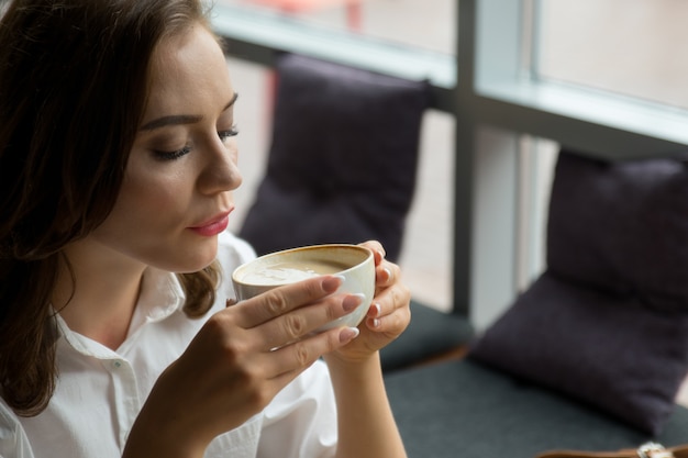 Chica guapa disfruta de un café fragante y un pastel dulce sentado en