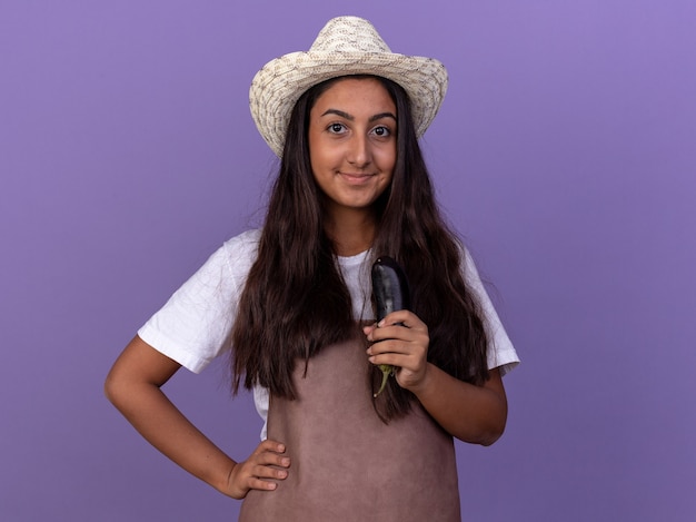 Chica Joven Jardinero En Delantal Y Sombrero De Verano Con Berenjena