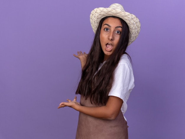 Chica Joven Jardinero En Delantal Y Sombrero De Verano Presentando Algo