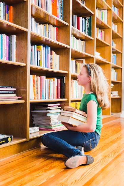 Chica con libros sentado en estanterías | Foto Gratis