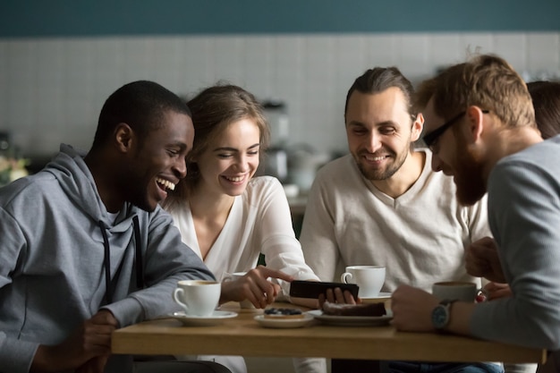 Chica milenaria que muestra videos móviles divertidos para amigos en un café Foto gratis