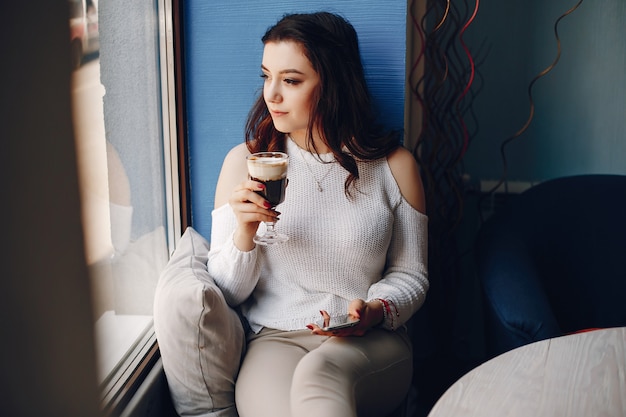 Chica en un suéter blanco sentado solo en la cafetería Foto gratis