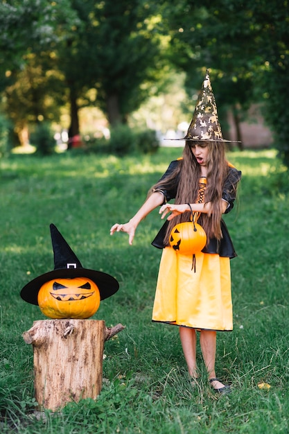 Chica En Traje De Bruja Mostrando Llegar Manos En Calabaza Foto Gratis