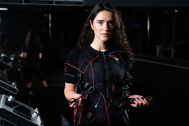 Chica en traje de ems en gimnasio entrenamiento deportivo en traje de estimulación muscular