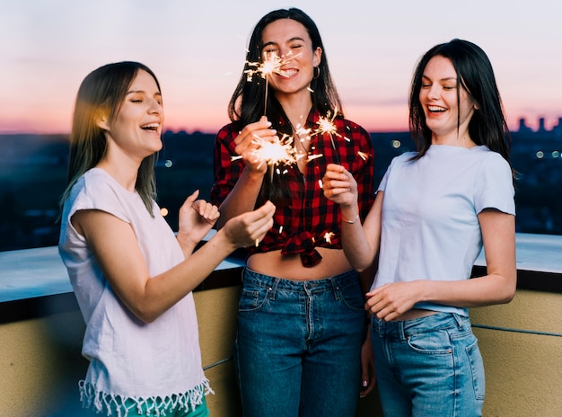 Chicas sosteniendo fuegos artificiales en la azotea al amanecer Foto gratis