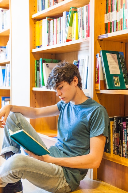 Chico adolescente leyendo en la biblioteca tranquila | Foto Gratis