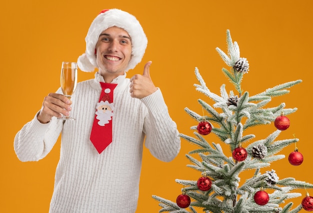 Chico Guapo Joven Alegre Con Sombrero De Navidad Y Corbata De Santa Claus De Pie Cerca Del árbol 1343