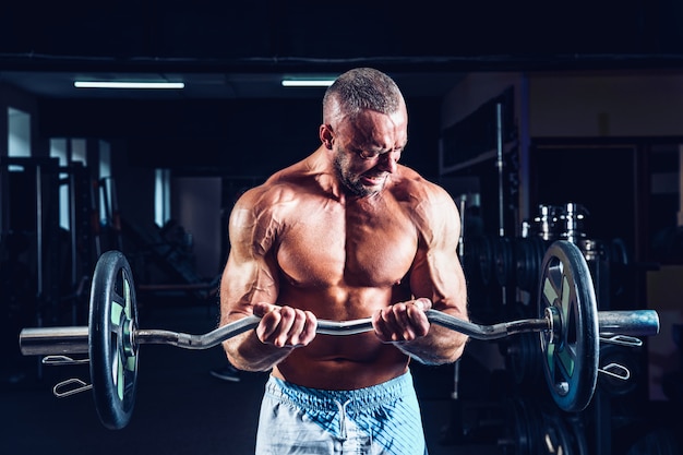 Chico musculoso culturista haciendo ejercicios en bíceps con pesas grandes en el gimnasio Foto