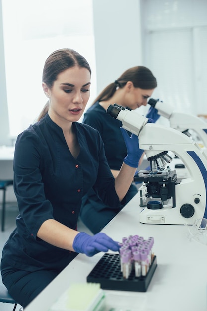 Científica de laboratorio femenina cuidadosa sentada cerca de su colega