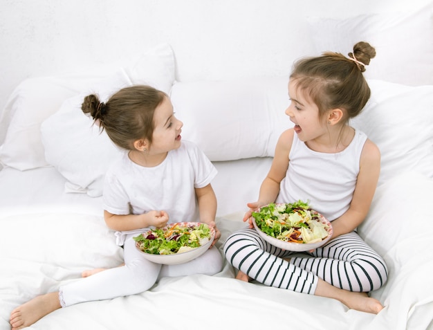 Comida sana en casa. felices dos niños lindos comiendo frutas y verduras en el dormitorio de la cama. alimentos saludables para niños y adolescentes. Foto gratis