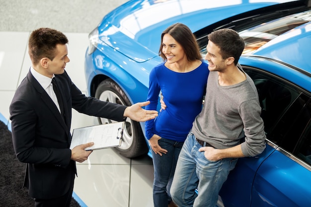 Comprando Su Primer Auto Juntos Vista De ángulo Alto Del Joven Vendedor De Automóviles De Pie 