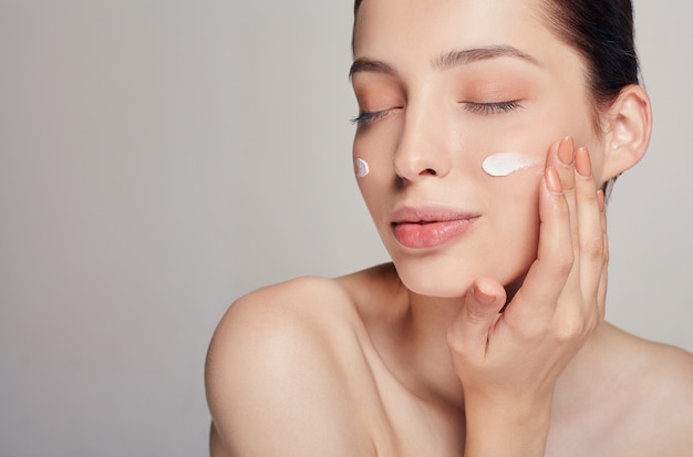 Concepto de belleza mujer hermosa joven con los ojos cerrados está aplicando crema cosmética en su rostro. cuidados en el hogar. protección de la piel. piel seca. | Foto Premium
